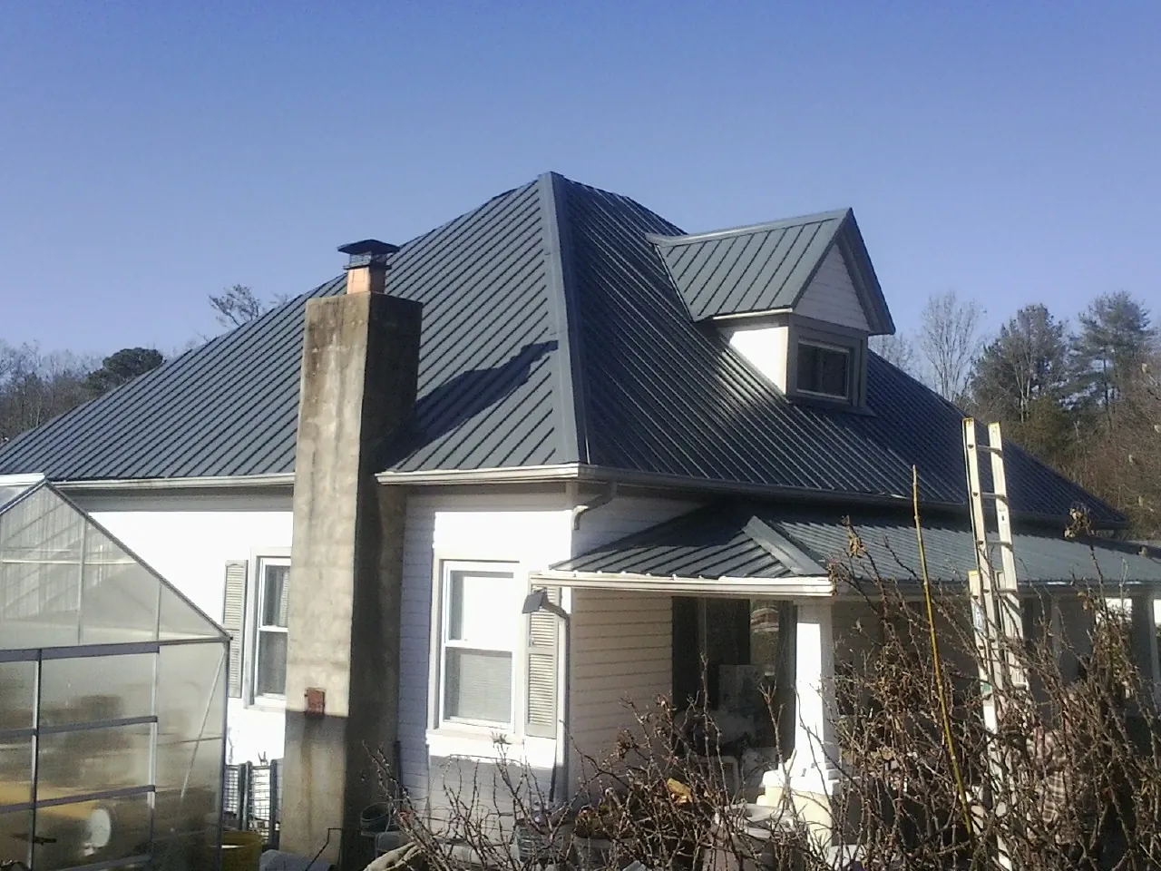 Dark blue standing seam metal roof on a white farmhouse with dormer — Slate & Tile Roof Repair by Roofing Brothers in Hillside