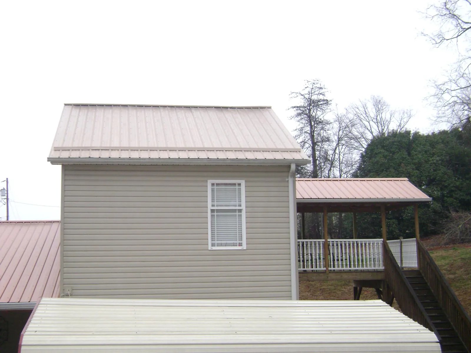 Tan metal roofs on a two story addition and attached porch, from a Roof Replacement job in Hillside